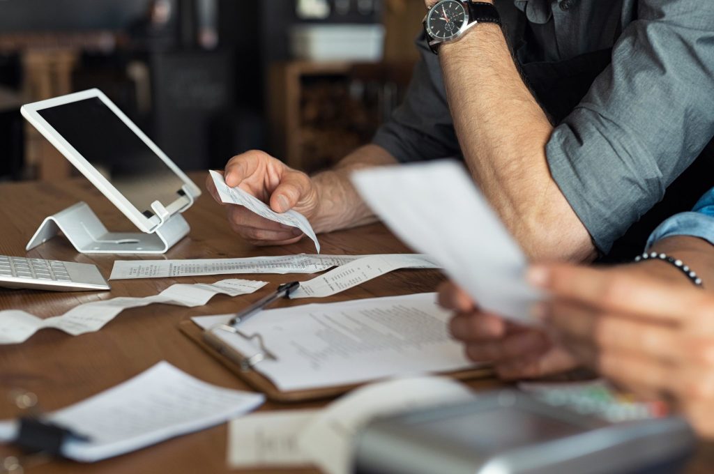 Image shows a desk with paperwork and an iPad and the arms of two people working through this.